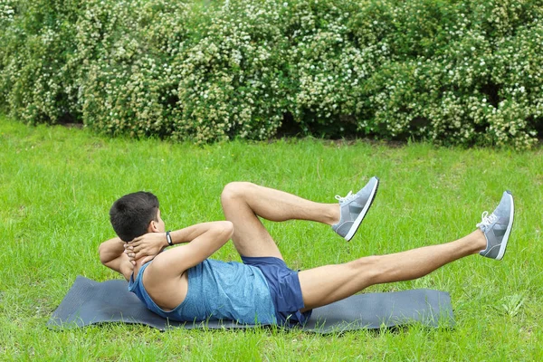 Lekkoatletycznego młody człowiek robi ćwiczenia crunch rowerów leżąc na macie na zewnątrz — Zdjęcie stockowe