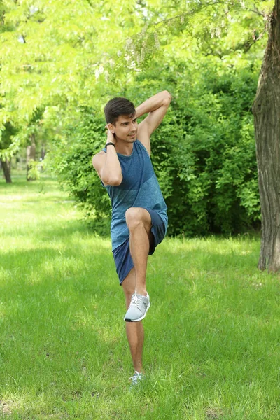 Athletic young man doing bicycle crunch exercise while standing on grass in green spring park — Stock Photo, Image