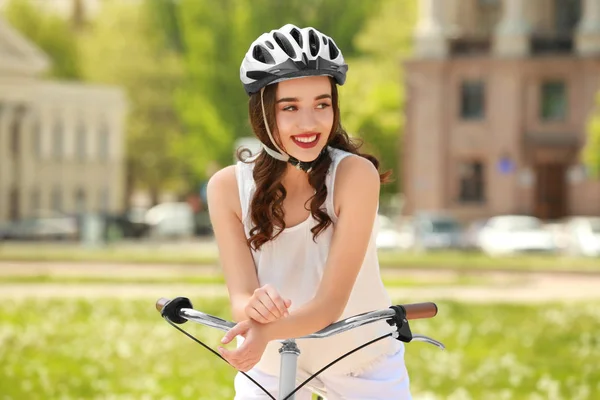 Mooie jonge vrouw met fiets en helm in park op zonnige dag — Stockfoto