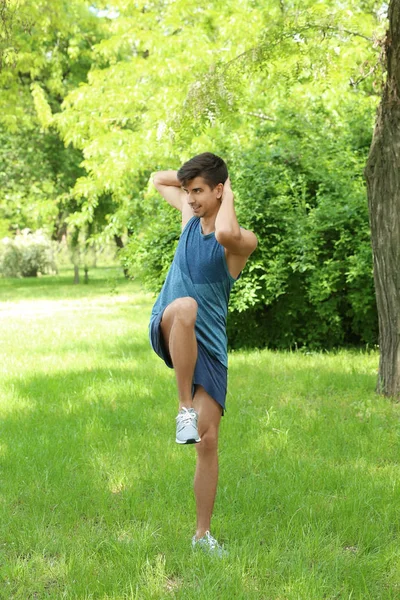 Yeşil Bahar park çimenlerin üzerinde dururken Bisiklet crunch egzersiz yaparak atletik genç adam — Stok fotoğraf