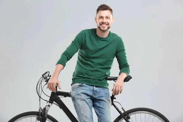 Bonito jovem com bicicleta no fundo claro — Fotografia de Stock