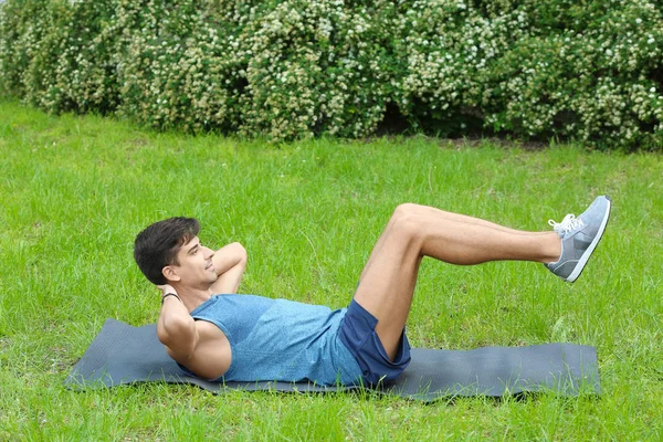 Atlético joven haciendo ejercicio crujiente bicicleta mientras está acostado en la estera al aire libre — Foto de Stock