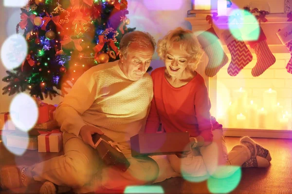 クリスマス暖炉のそばに座ってながらプレゼントを開く老夫婦 — ストック写真