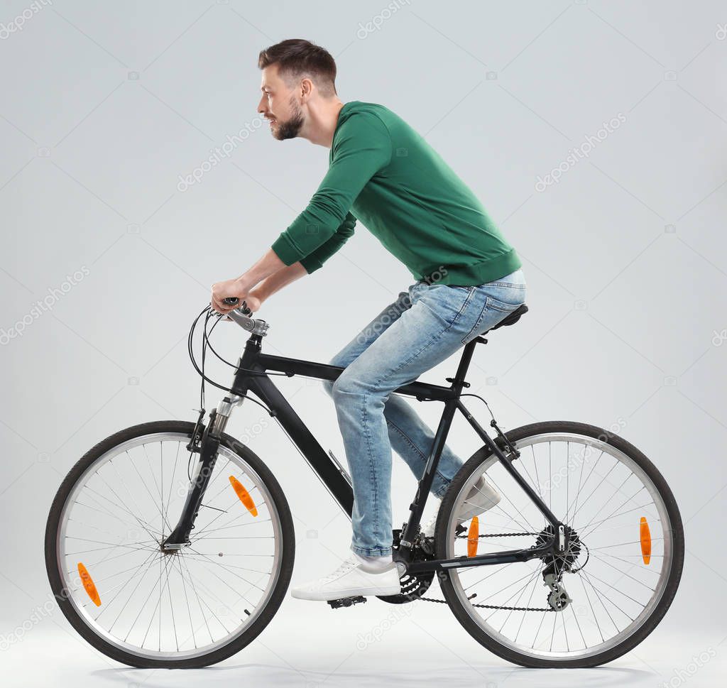 Handsome young man riding bicycle on light background