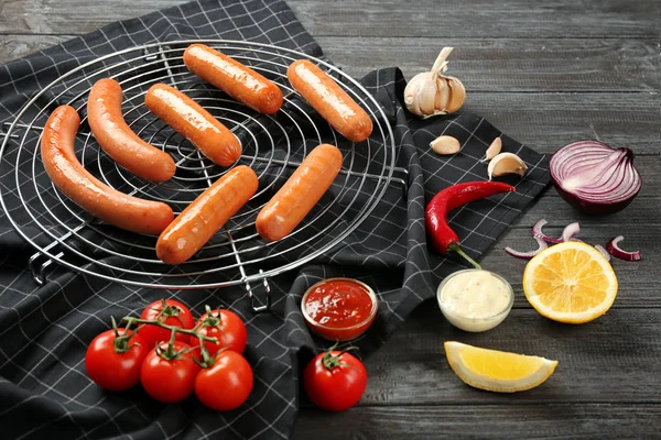Composition with yummy sausages on cooling grid with vegetables and sauce on wooden table — Stock Photo, Image