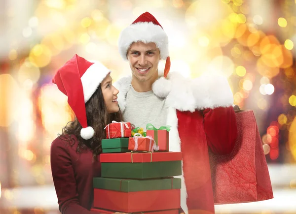 Jeune couple avec des achats de Noël sur fond de lumières floues — Photo