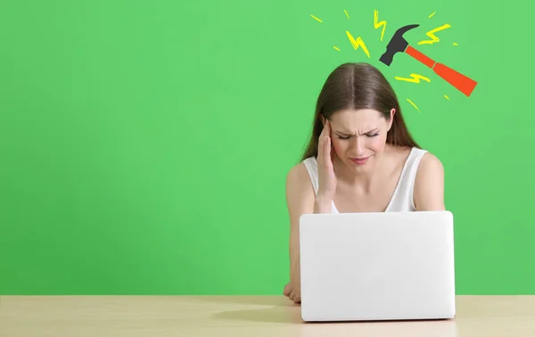 Молода жінка, яка страждає від головного болю під час роботи з ноутбуком та малюванням молотка на кольоровому фоні — стокове фото