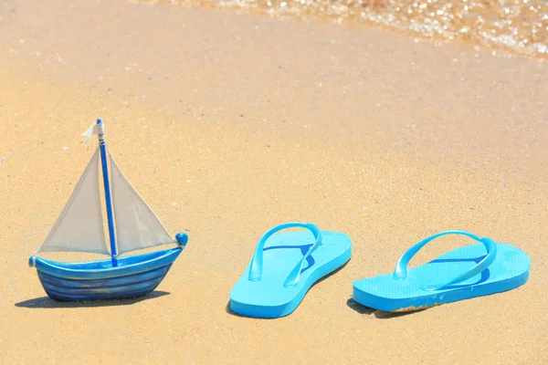 人字拖鞋和玩具船在沙滩上 — 图库照片