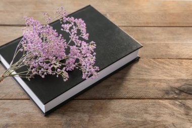 Kitap ahşap arka plan üzerine boş siyah kapak ve güzel çiçekler