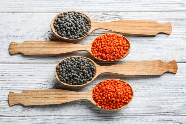 Spoons with red and black lentils on wooden background — Stock Photo, Image