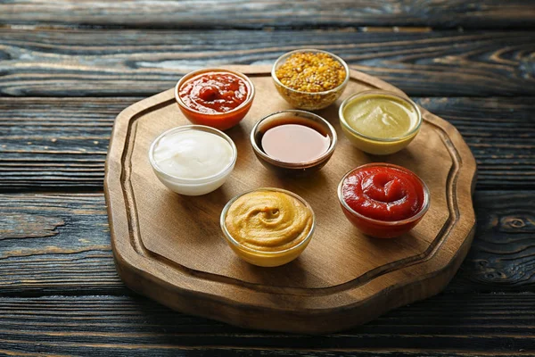 Placa de madera con diferentes salsas en la mesa —  Fotos de Stock