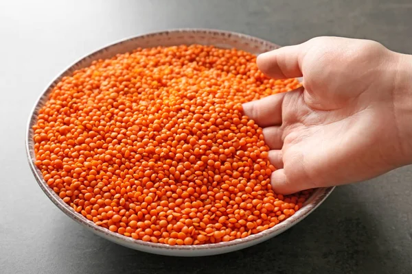 Female hand with red lentils in bowl on grey background — Stock Photo, Image