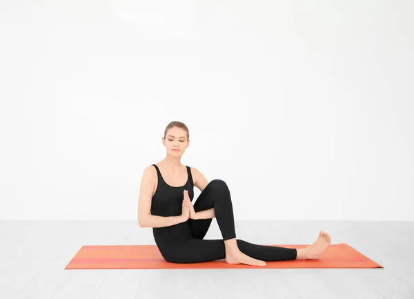 Joven hermosa mujer practicando yoga pose cerca de la pared blanca en el interior —  Fotos de Stock