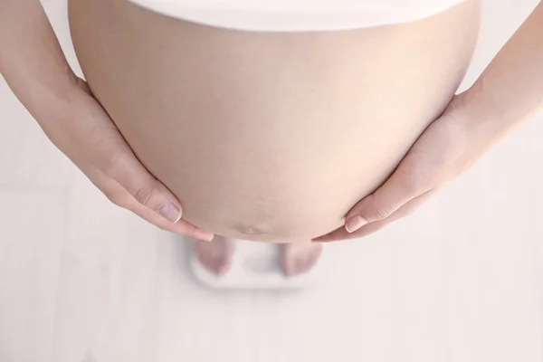 Pregnant woman standing on scales at home. Pregnancy weight gain concept