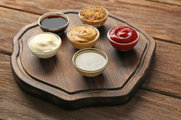 Деревянная тарелка с различными соусами на столе — стоковое фото