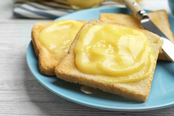 Plate with fresh toasts and delicious lemon curd on wooden table, closeup — Stock Photo, Image