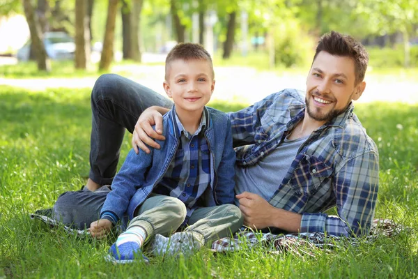 Vater und Sohn sitzen an sonnigem Tag auf dem Rasen im Park — Stockfoto