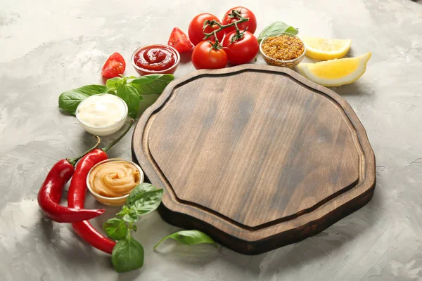 Placa de madera, diferentes salsas y verduras sobre fondo grunge — Foto de Stock