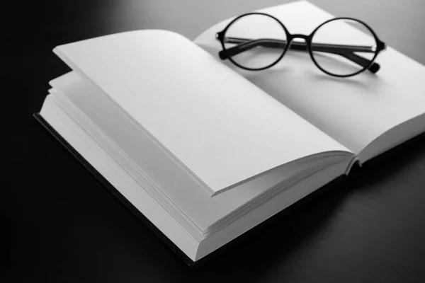 Open book with blank pages and glasses on black background — Stock Photo, Image