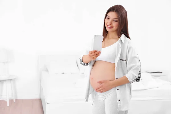Vacker gravid kvinna med mobiltelefon hemma — Stockfoto