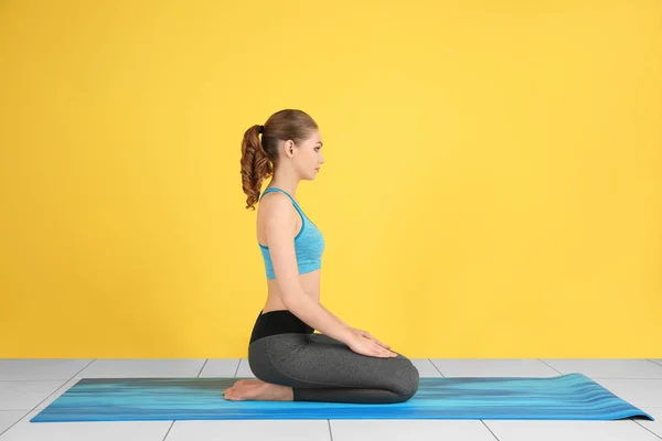 Joven hermosa mujer practicando yoga pose cerca de la pared de color en el interior — Foto de Stock