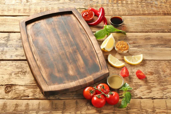Houten plank, verschillende sauzen en groenten op tafel — Stockfoto