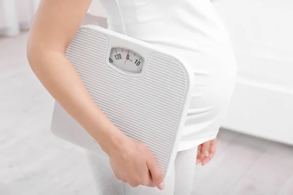 Pregnant woman with scales at home. Pregnancy weight gain concept