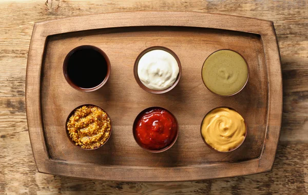 Houten plaat met verschillende sauzen op tafel — Stockfoto
