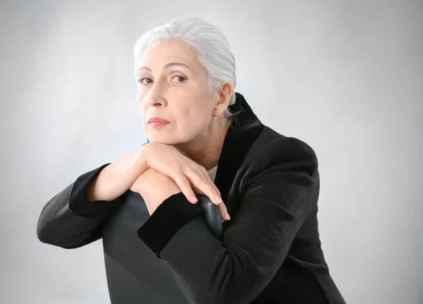 Schöne elegante ältere Frau sitzt auf Stuhl vor grauem Hintergrund — Stockfoto