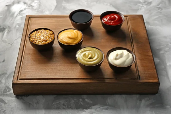 Wooden board with different sauces on grunge background — Stock Photo, Image