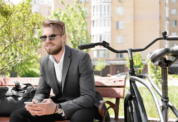 Jongeman met telefoon terwijl hij op de bank zit met de fiets in het park — Stockfoto