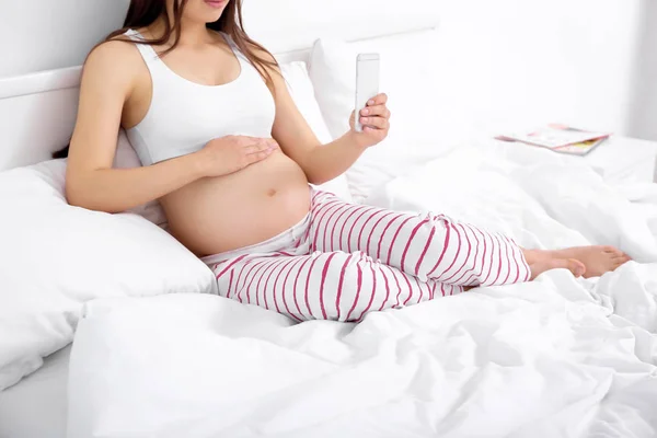 Mulher grávida com telefone celular sentado na cama — Fotografia de Stock