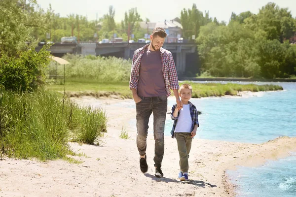 Dad and son walking near river on sunny day — Stock Photo, Image