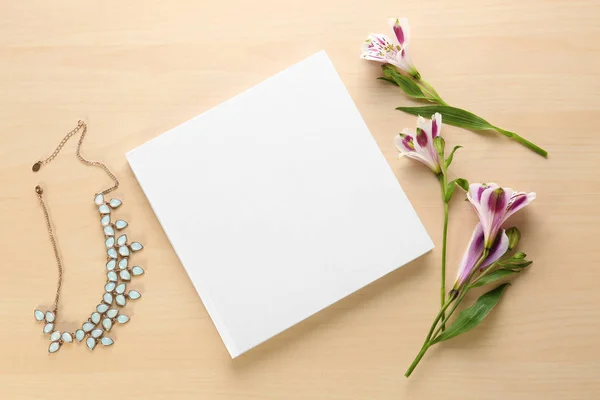Boek met lege witte cover, ketting en mooie bloemen op lichte houten achtergrond — Stockfoto