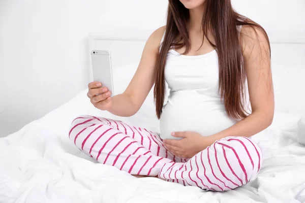 Mulher grávida com telefone celular sentado na cama — Fotografia de Stock