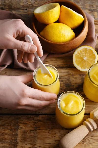 Femme prenant du citron caillé dans un bocal en verre sur un fond en bois — Photo