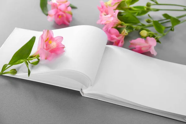 Libro abierto con páginas en blanco y hermosas flores sobre fondo gris — Foto de Stock