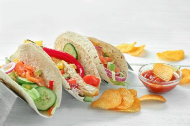 Stand with tasty fish tacos on white wooden background clipart
