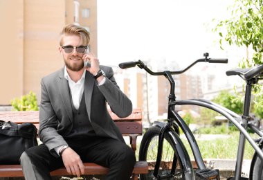 Bisiklet park ile bankta otururken telefonla konuşan genç adam