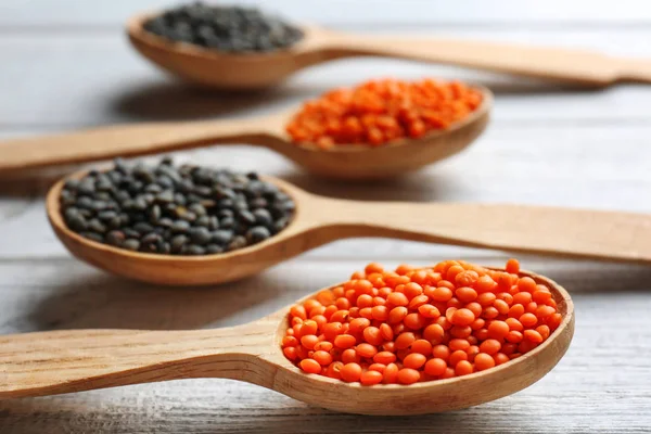 Cucchiai con lenticchie rosse e nere su fondo di legno — Foto Stock