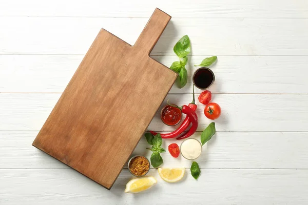 Composición con tabla de madera, diferentes salsas y verduras en la mesa —  Fotos de Stock