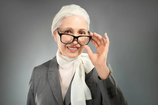 Piękne eleganckie starszą kobietę w okularach na szarym tle — Zdjęcie stockowe