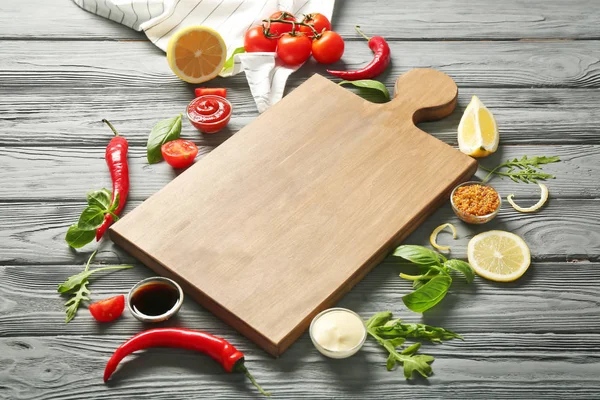 Composición con tabla de madera, diferentes salsas y verduras en la mesa —  Fotos de Stock