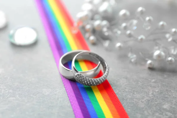 Anelli in argento per matrimonio lesbico e nastro arcobaleno su tavolo grigio — Foto Stock