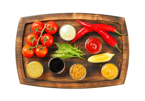 Houten plaat met verschillende sauzen en groenten op witte achtergrond — Stockfoto
