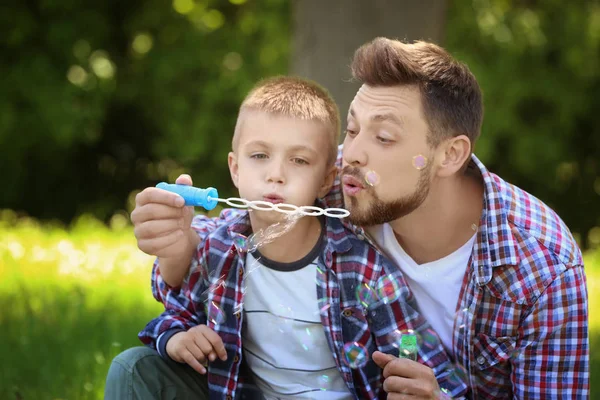 Pappa och son blåser bubblor i parken på solig dag — Stockfoto