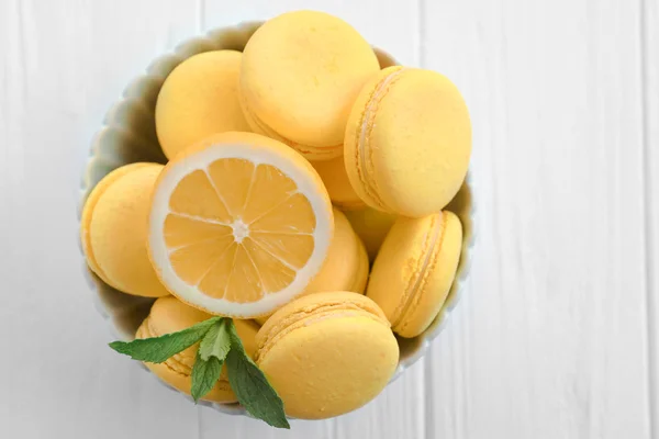 Bol avec de savoureux macarons au citron sur une table en bois blanc — Photo