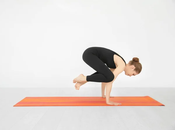 Mooie jongedame het beoefenen van yoga houding in de buurt van witte muur binnenshuis — Stockfoto