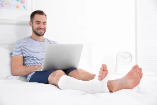 Homme avec ordinateur portable et jambe bandée — Photo