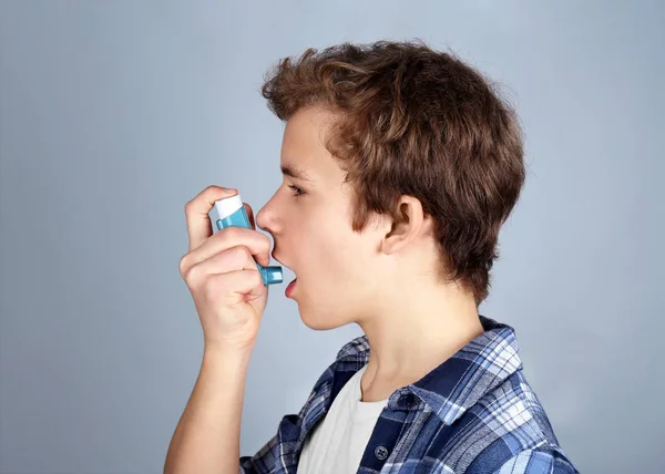 Młody chłopak za pomocą inhalatora astmy i chorób układu oddechowego, na jasnym tle — Zdjęcie stockowe
